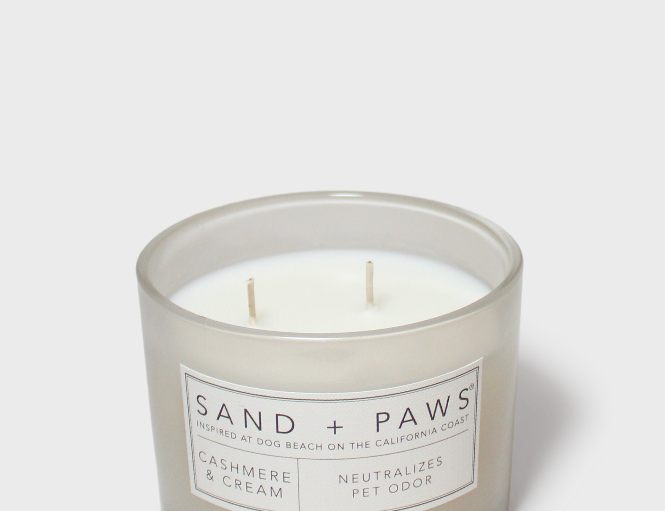 Sand + Paws scented candle jar with cream wax, two wicks, 'SAND + PAWS' label
