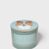 Scented candle with dog graphic lid and 'SAND + PAWS' label on light-blue jar