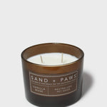 Scented candle in dark glass jar with lit wicks and Sand + Paws label