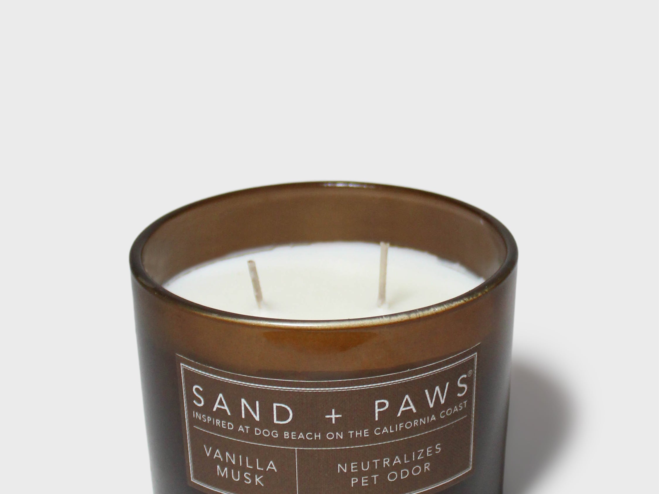 Scented candle in dark glass jar with lit wicks and Sand + Paws label