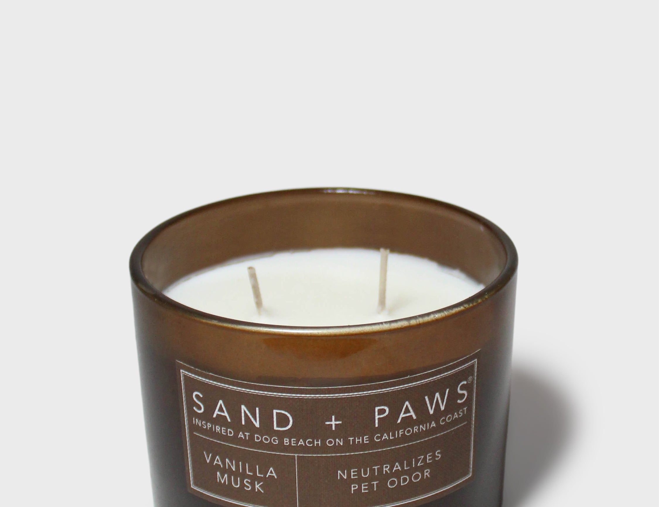 Scented candle in dark glass jar with lit wicks and Sand + Paws label