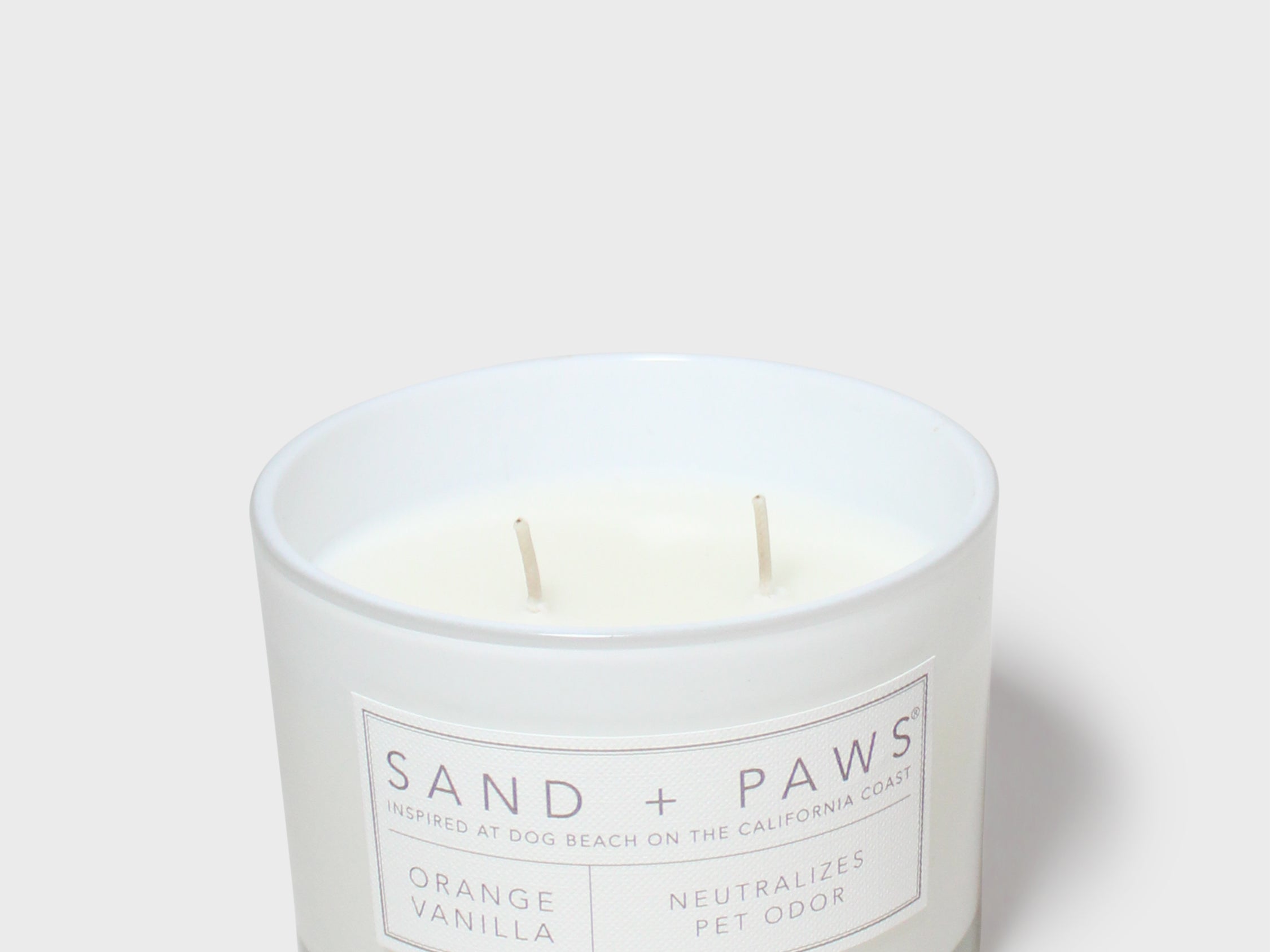 Scented candle in white glass jar with two wicks and orange vanilla label