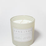 Scented candle tin with 'Sand + Fog' label and two wicks