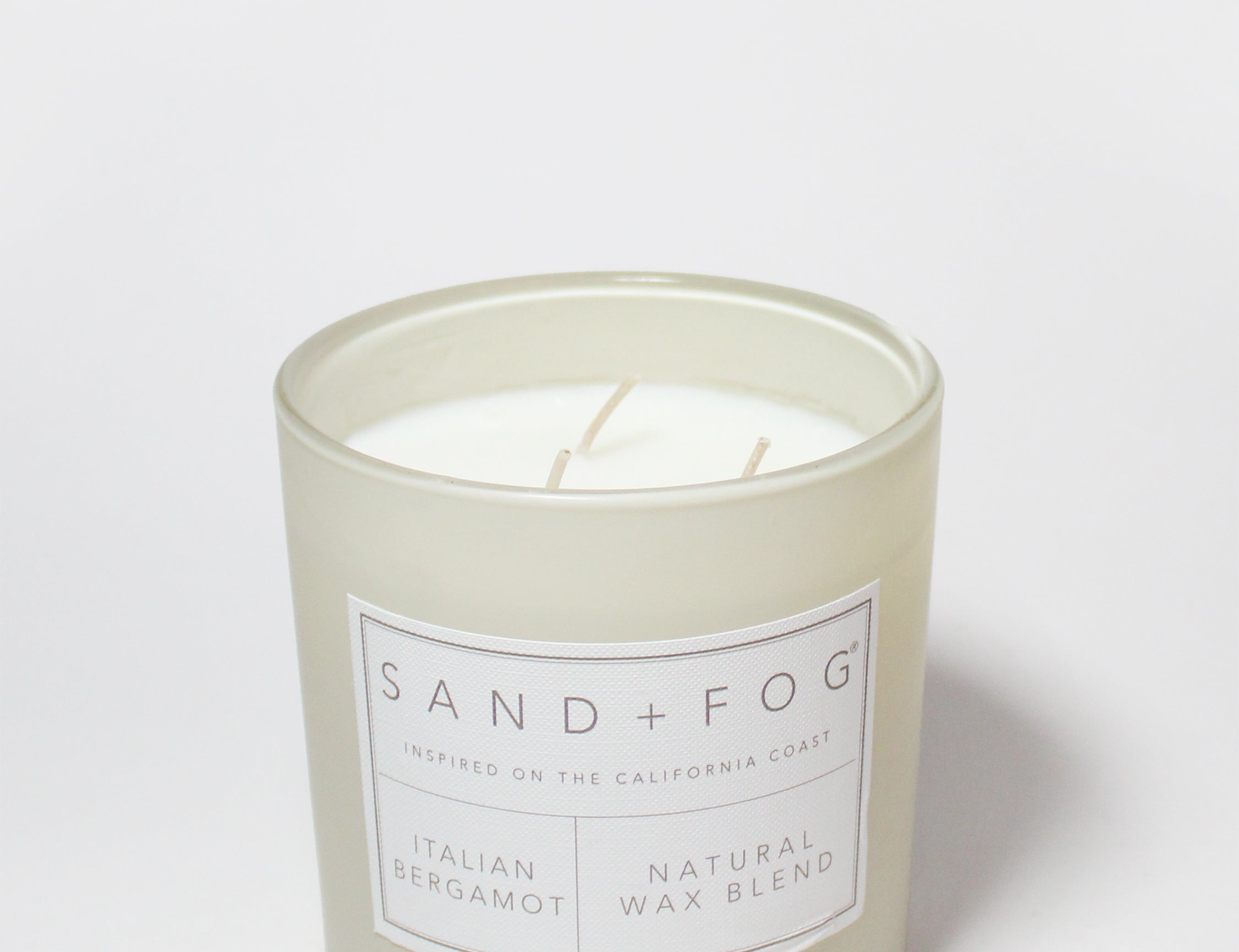 Scented candle tin with 'Sand + Fog' label and two wicks
