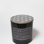 Scented candle jar with patterned lid and SAND + FOG label on black glass