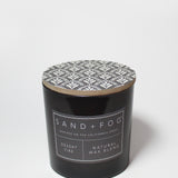 Scented candle jar with patterned lid and SAND + FOG label on black glass