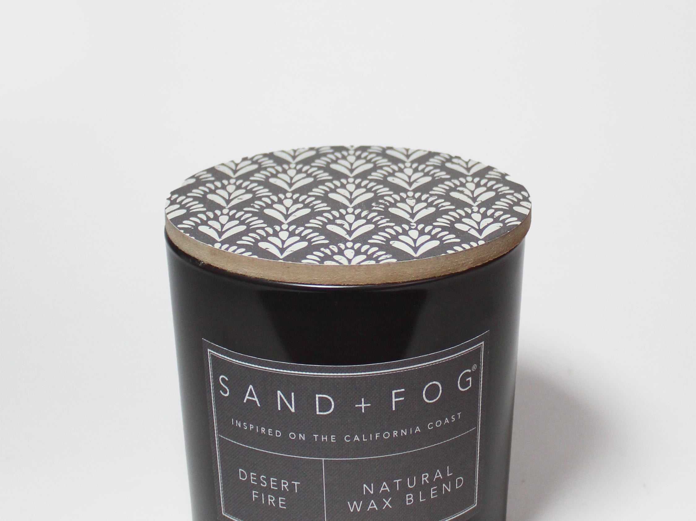 Scented candle jar with patterned lid and SAND + FOG label on black glass