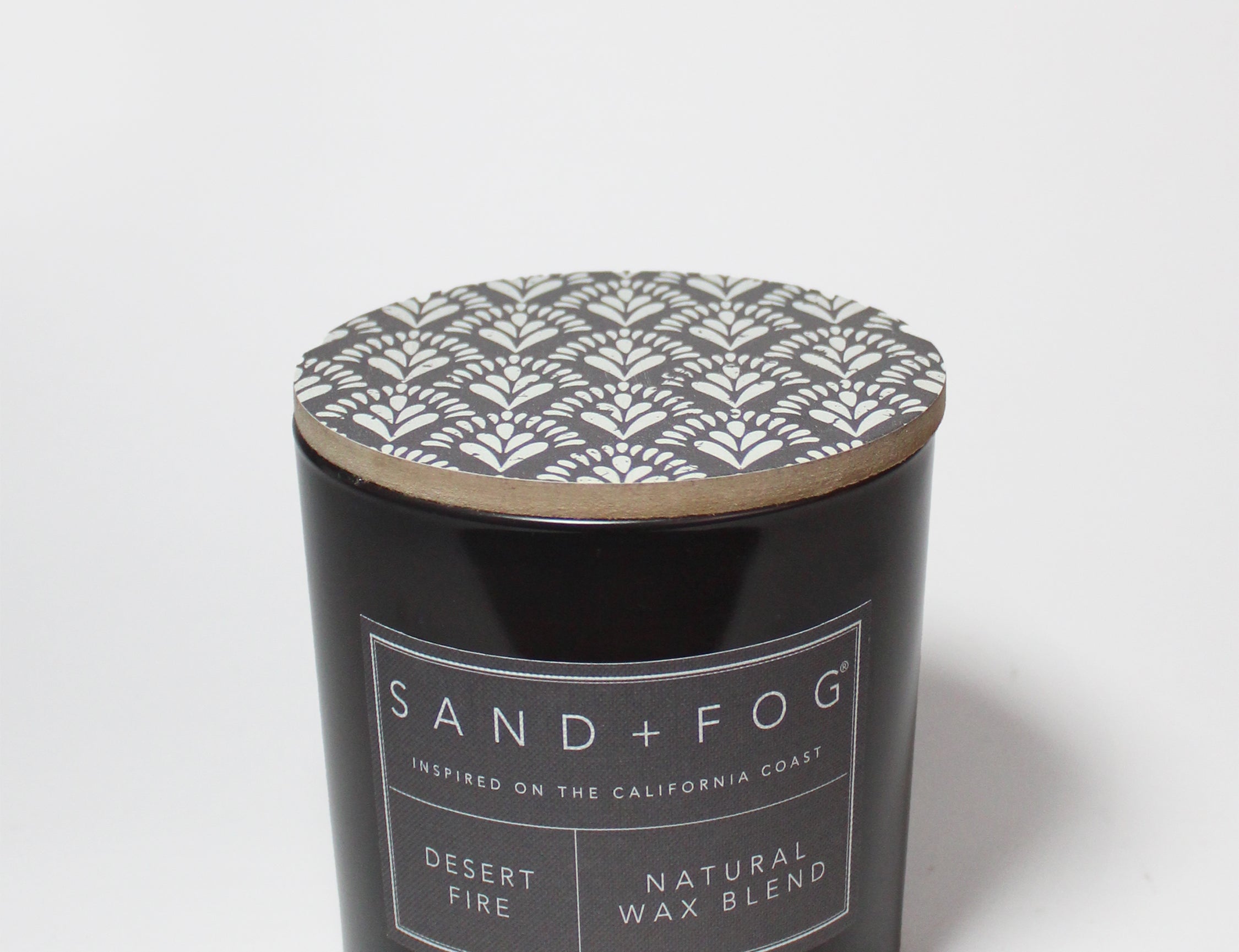 Scented candle jar with patterned lid and SAND + FOG label on black glass
