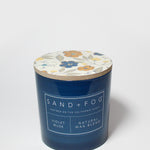 Blue scented candle with floral lid and SAND+FOG label