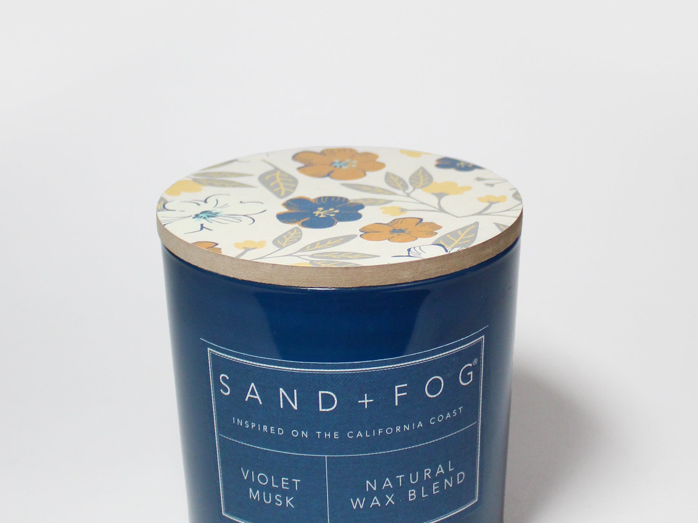 Blue scented candle with floral lid and SAND+FOG label