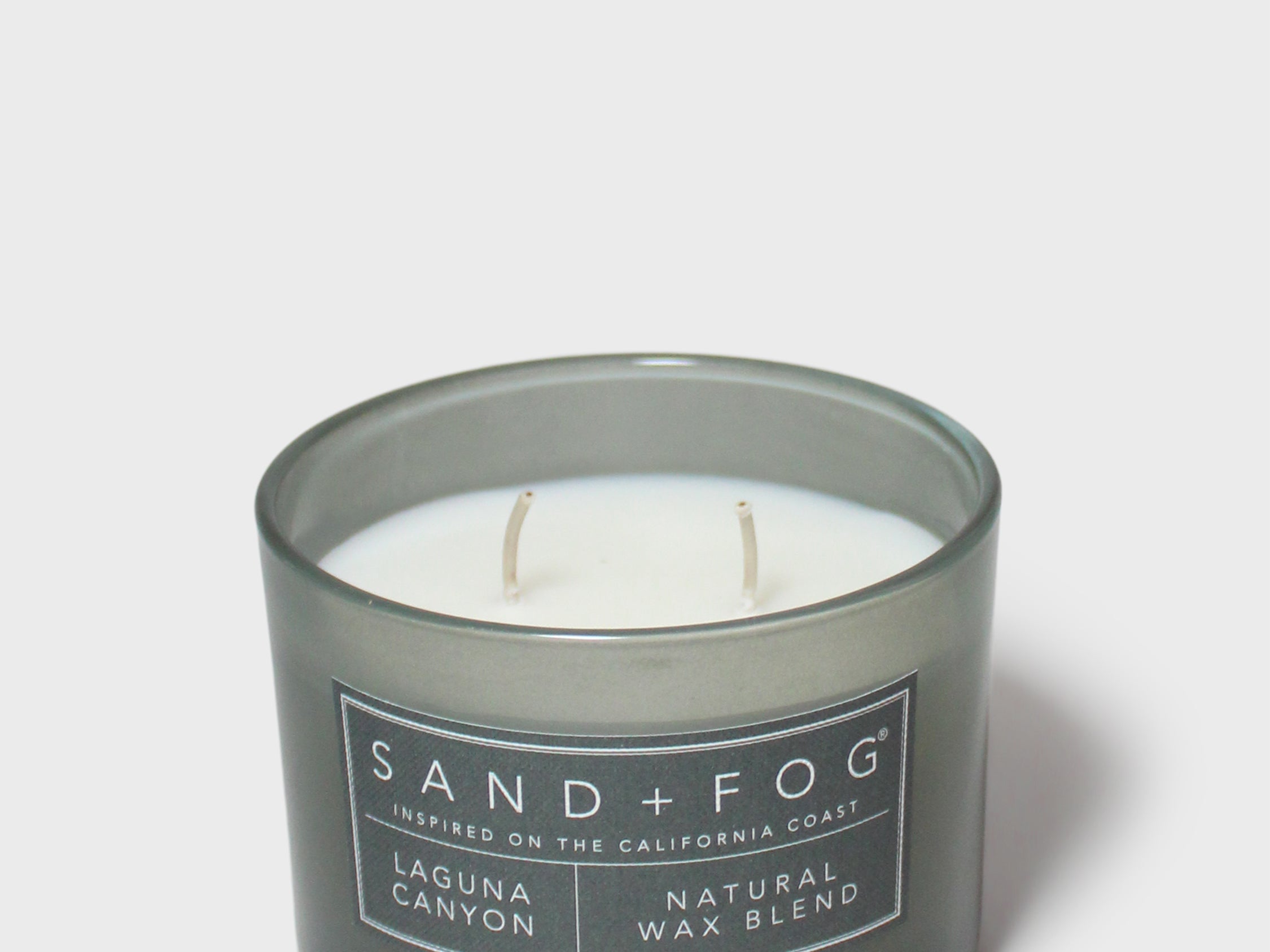 Scented candle in dark glass jar with white label and two visible wicks