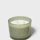 Scented candle in green glass jar with two wicks and Sand+Fog label