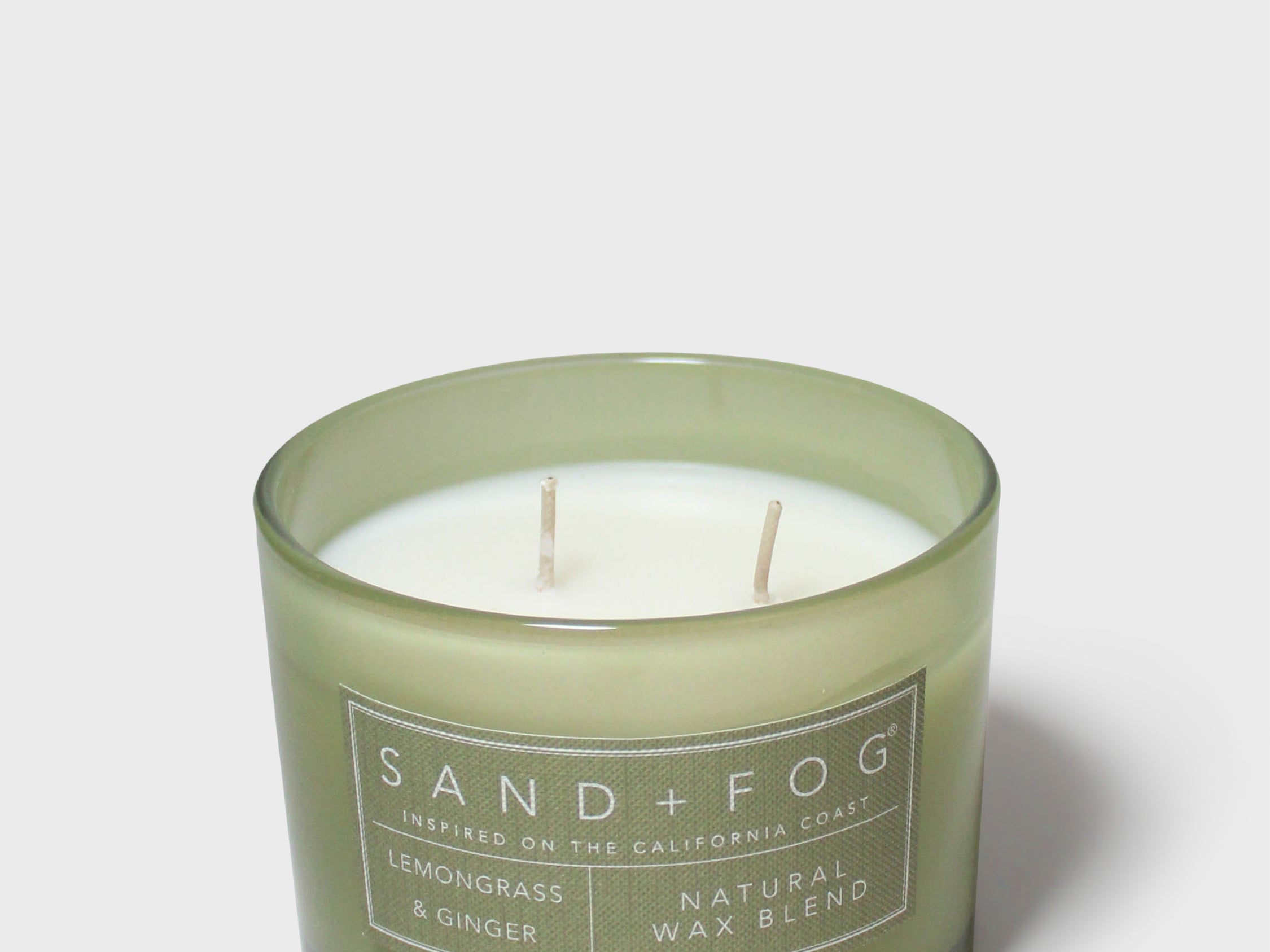 Scented candle in green glass jar with two wicks and Sand+Fog label