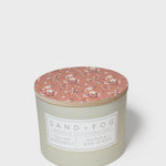 Round scented candle with terracotta floral lid and pale cream jar, front label visible