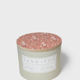 Round scented candle with terracotta floral lid and pale cream jar, front label visible