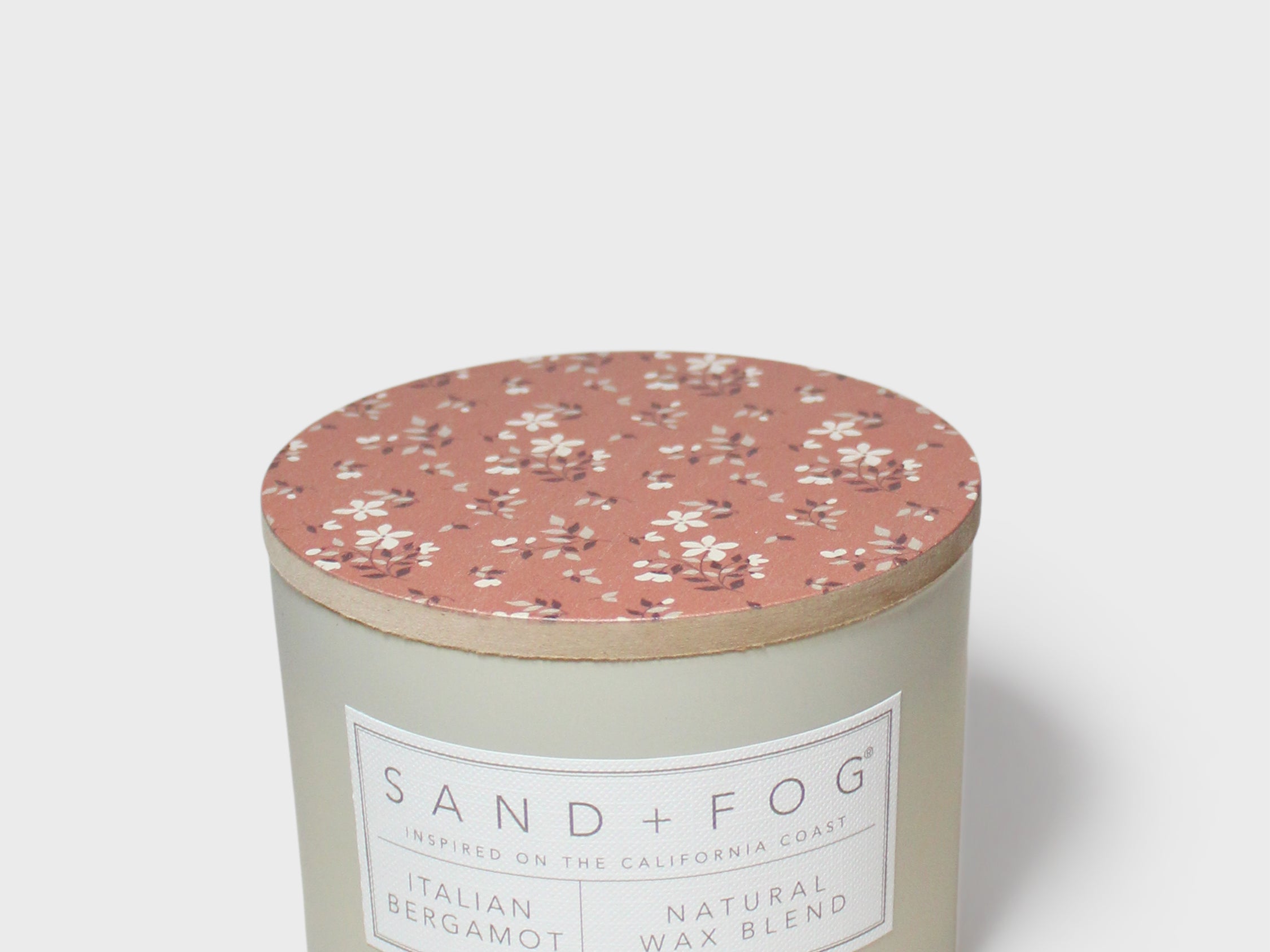 Round scented candle with terracotta floral lid and pale cream jar, front label visible