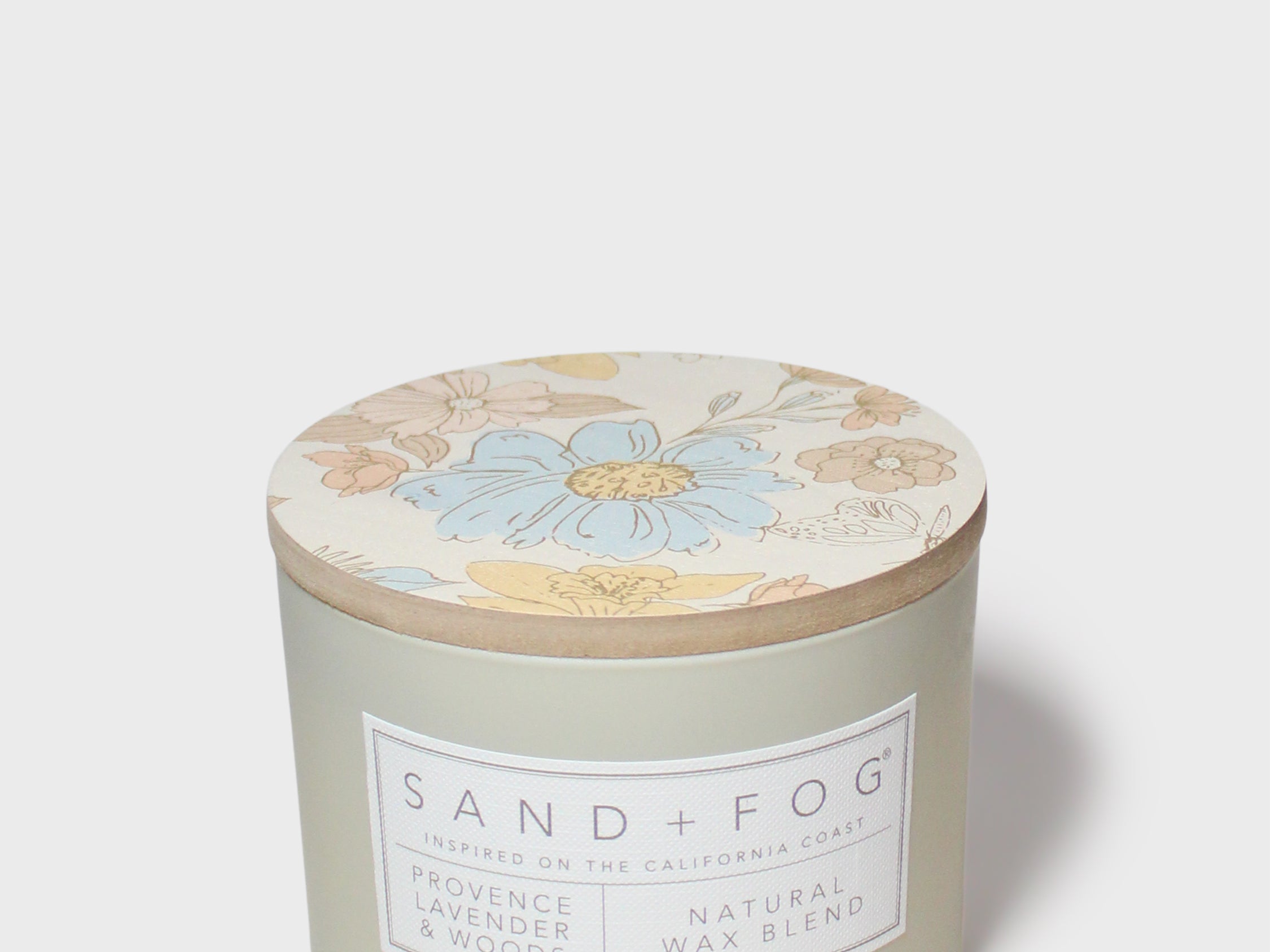 Scented candle with floral lid top and SAND+FOG label on frosted green jar