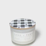 Scented candle jar with “Sand + Paws” label and plaid wood lid with paw prints