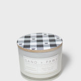 Scented candle jar with “Sand + Paws” label and plaid wood lid with paw prints