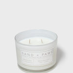 Scented glass jar candle with “Sand + Paws” label and two wicks