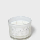 Scented glass jar candle with “Sand + Paws” label and two wicks
