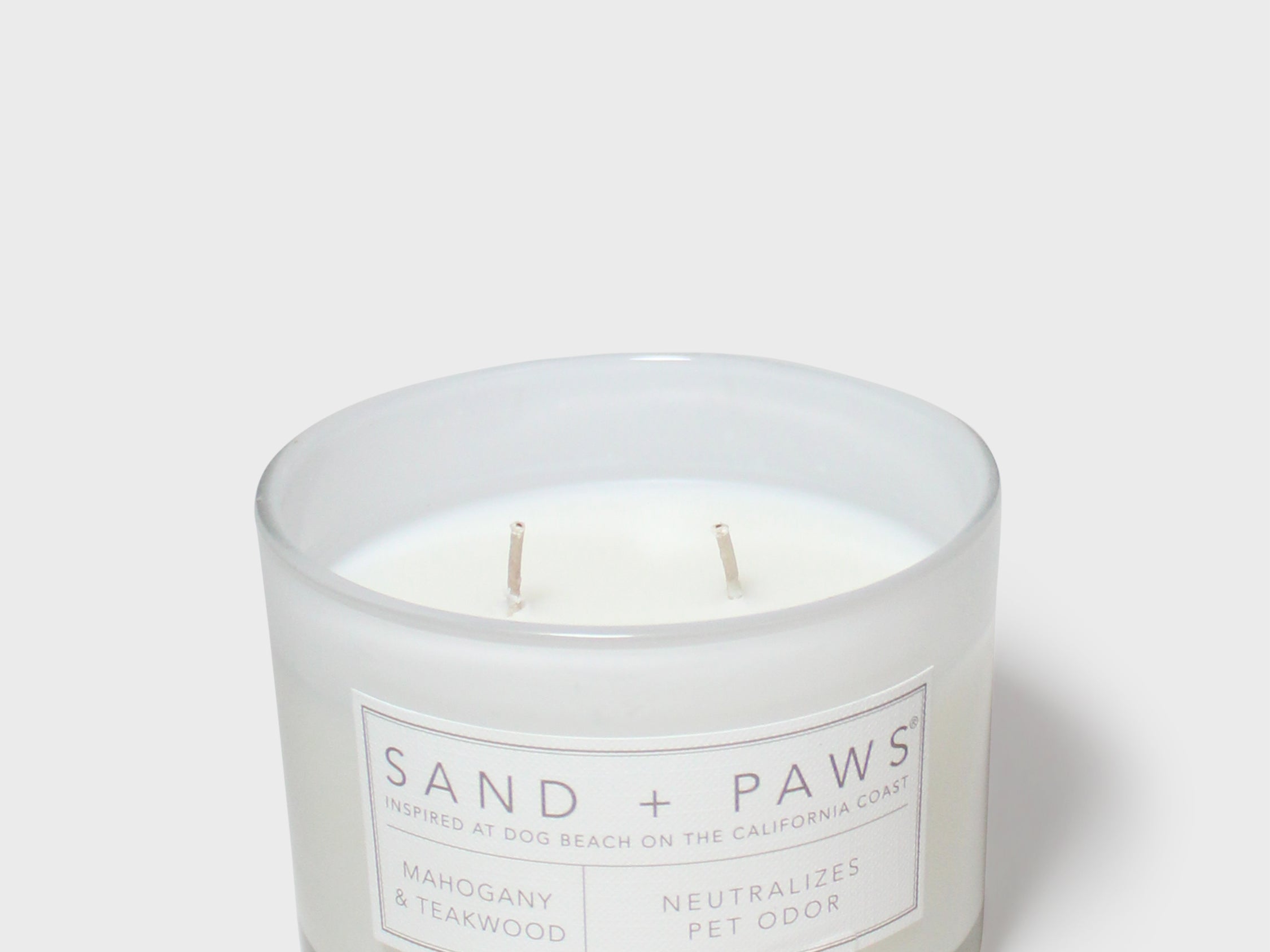 Scented glass jar candle with “Sand + Paws” label and two wicks