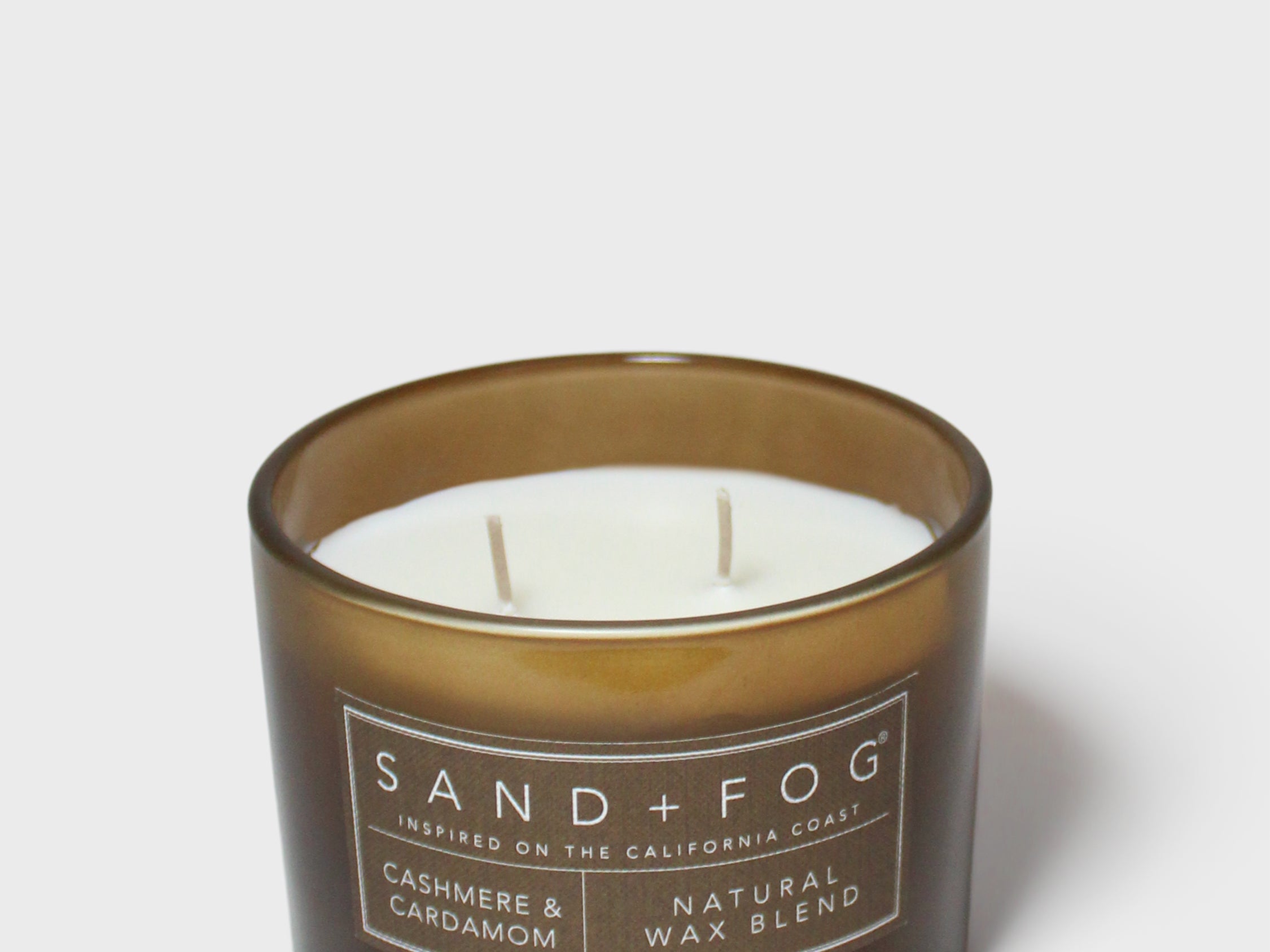 Brown scented candle in glass jar with white wax and SAND+FOG label