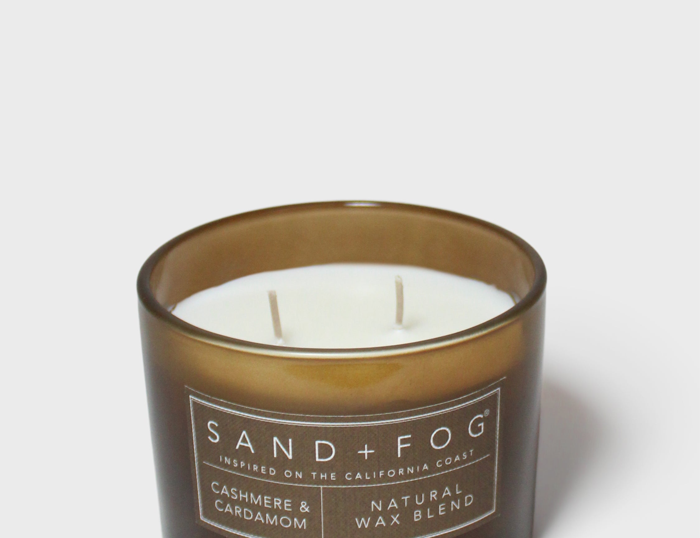 Brown scented candle in glass jar with white wax and SAND+FOG label