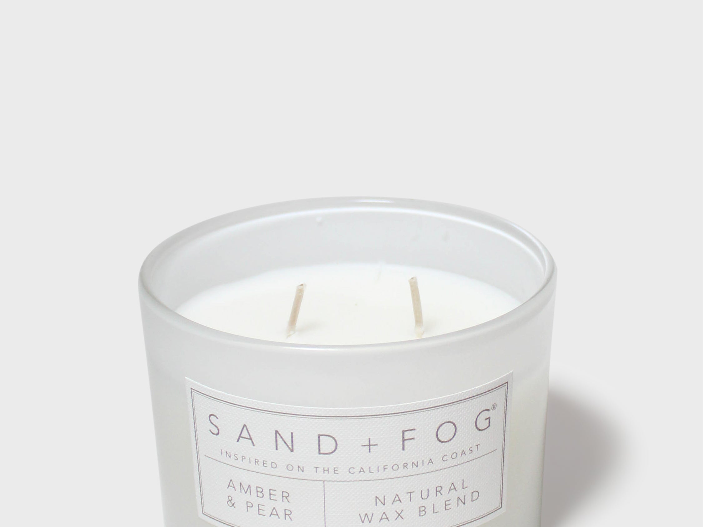 Scented candle in frosted glass jar with two wicks and SAND+FOG Amber & Pear label