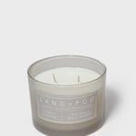 Scented candle in gray glass jar with visible wicks and “SAND+FOG” label