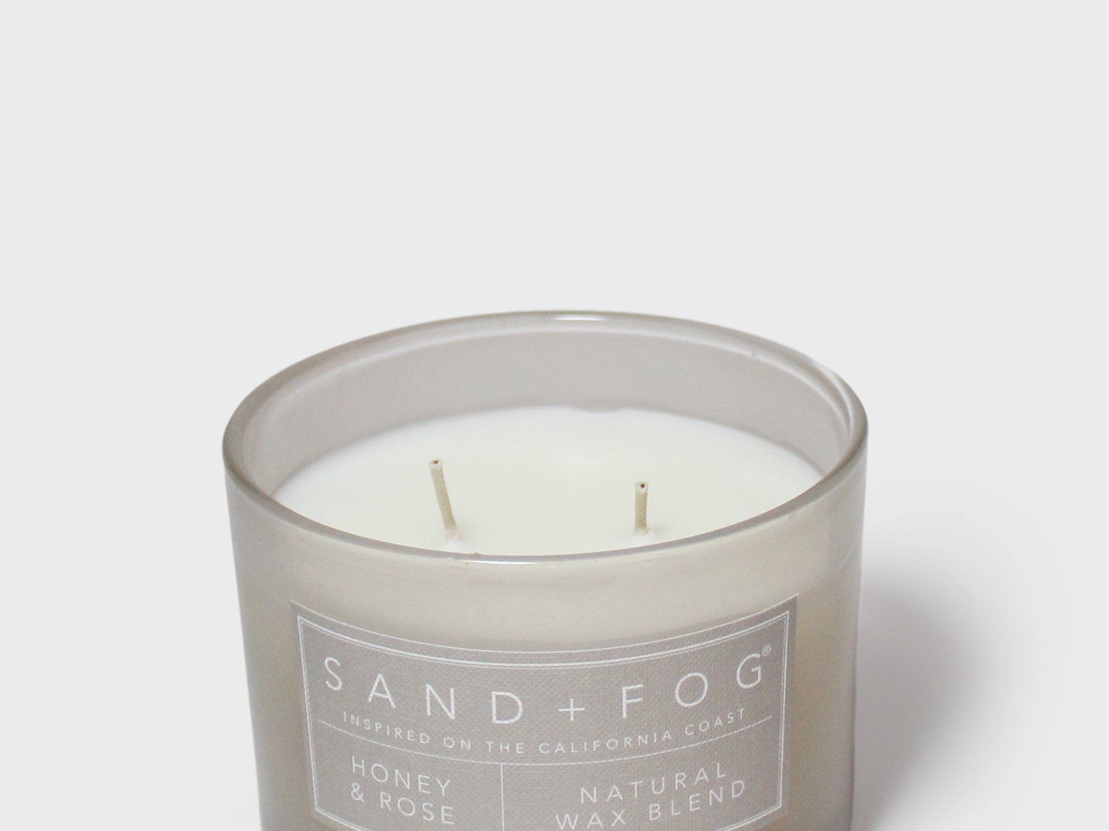 Scented candle in gray glass jar with visible wicks and “SAND+FOG” label
