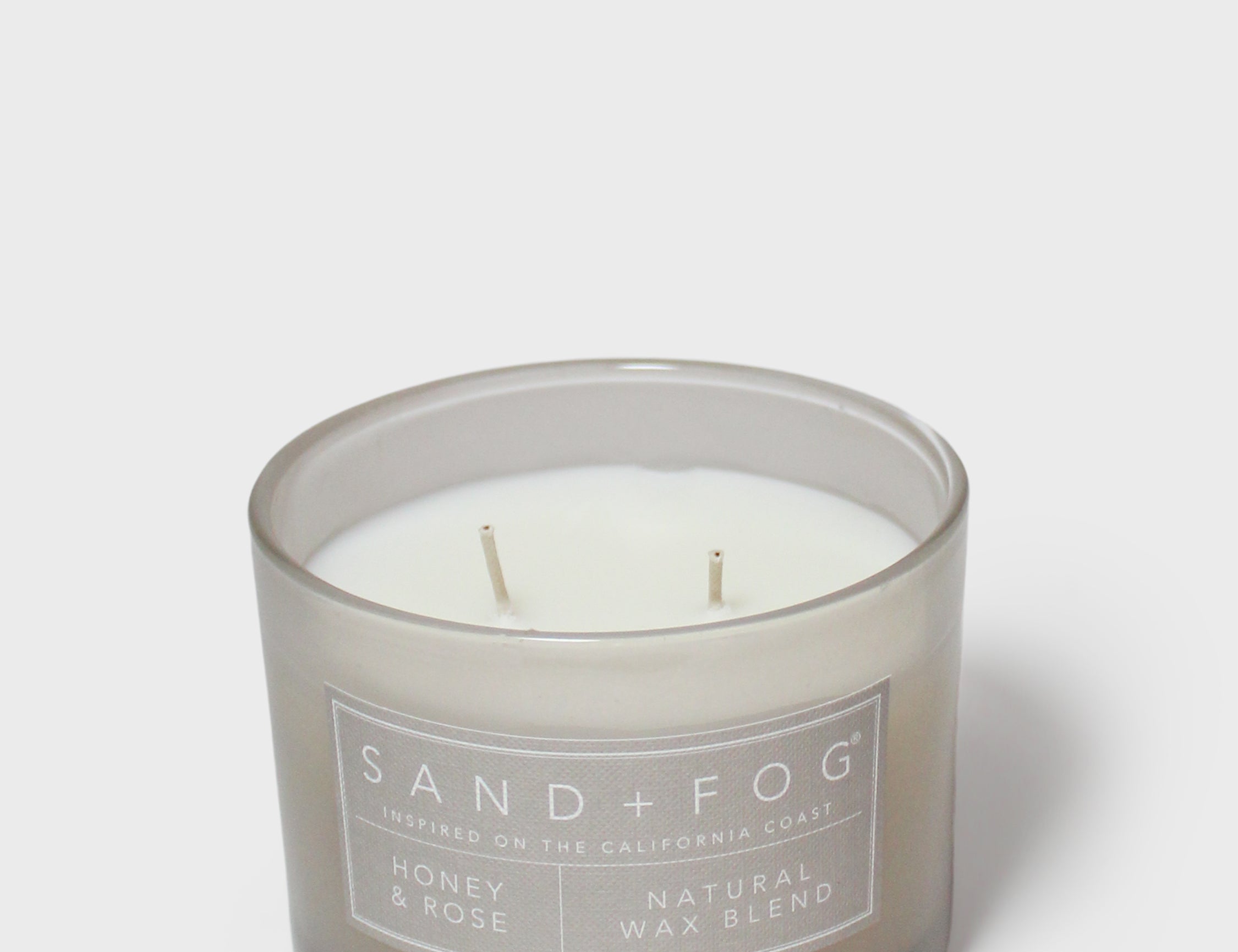 Scented candle in gray glass jar with visible wicks and “SAND+FOG” label