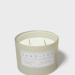 SAND + FOG scented candle in light gray glass jar with two visible wicks and label