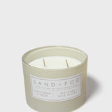 SAND + FOG scented candle in light gray glass jar with two visible wicks and label
