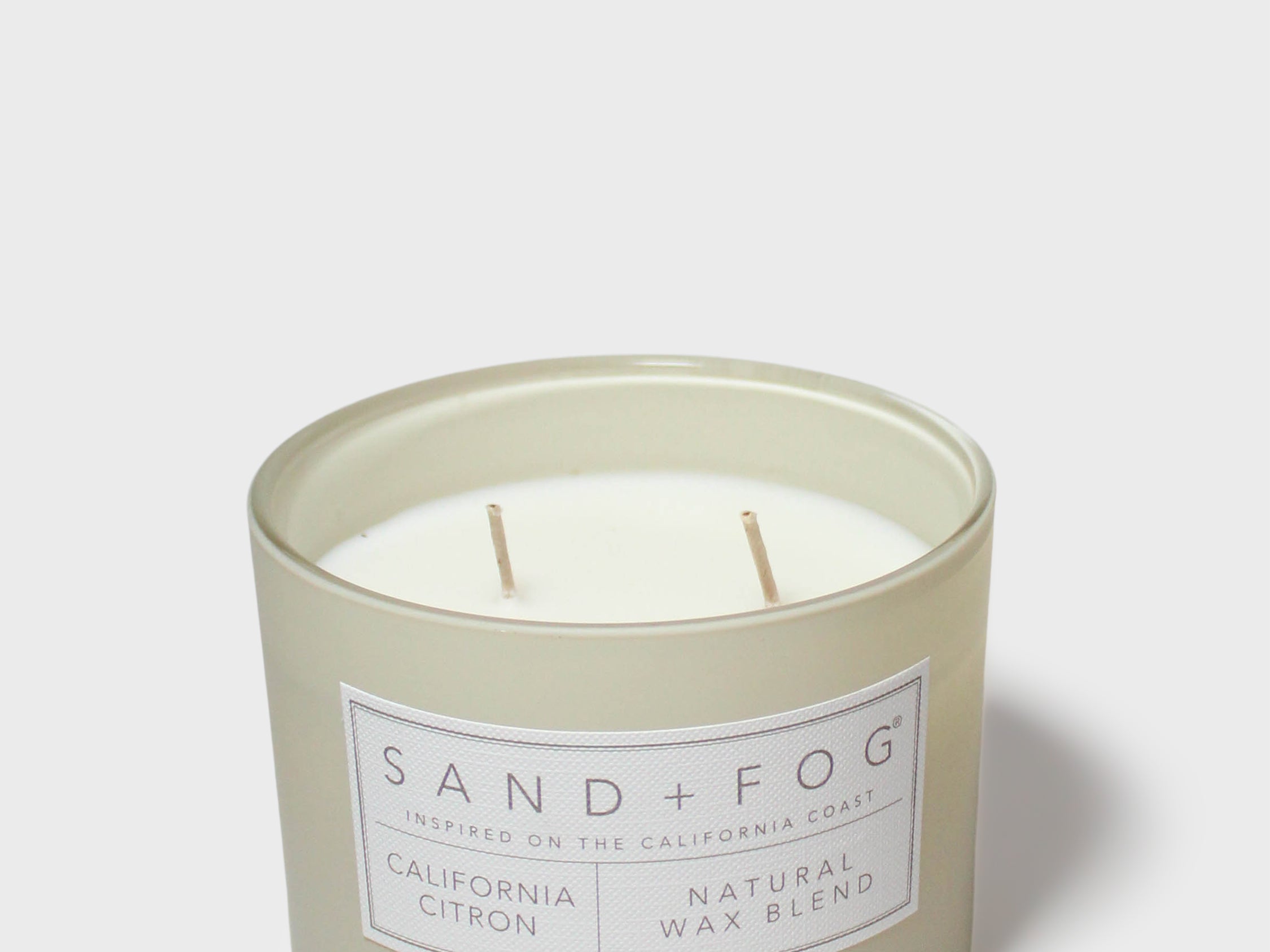 SAND + FOG scented candle in light gray glass jar with two visible wicks and label