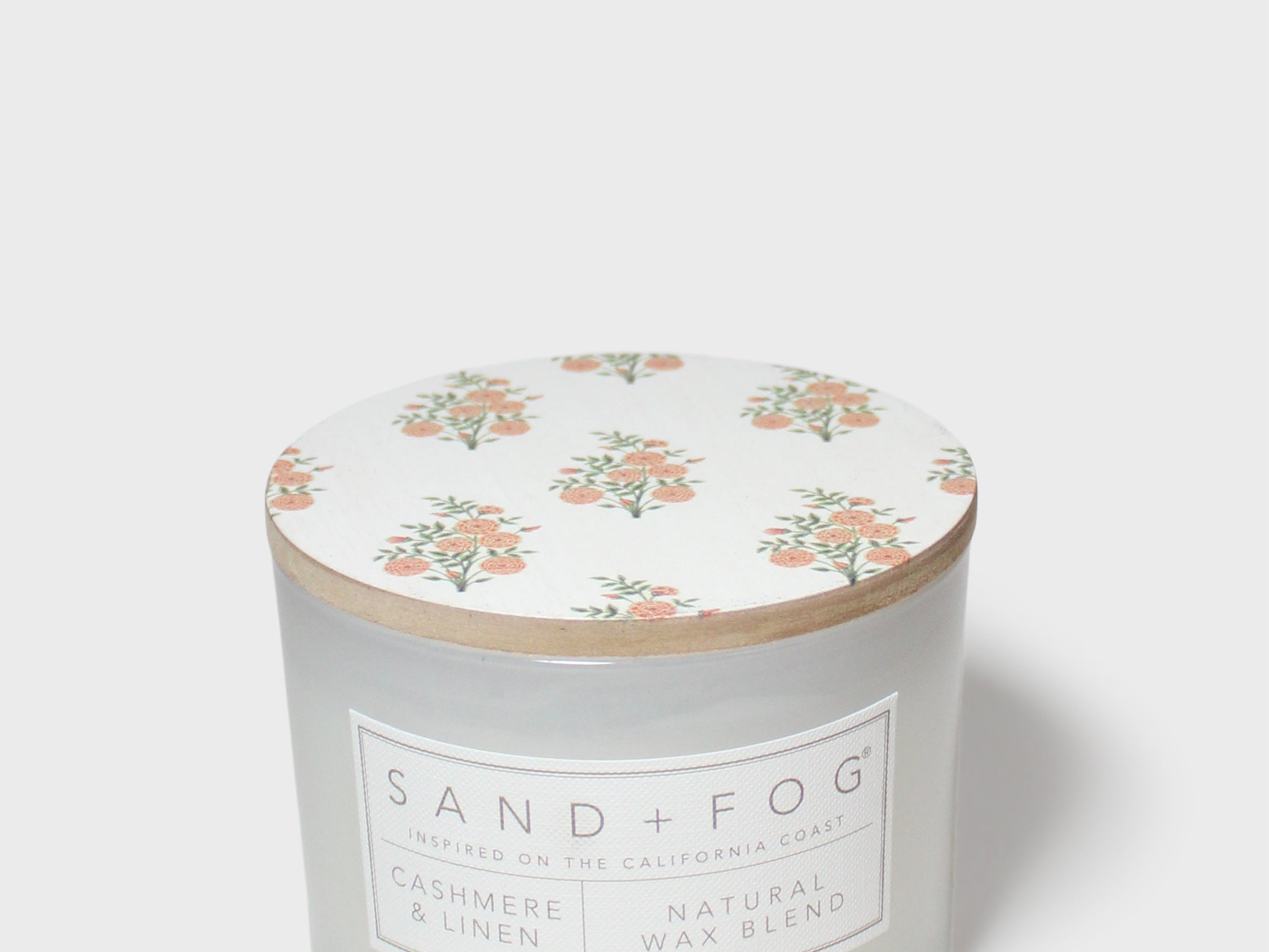 Scented candle jar with floral top and Sand + Fog wax blend label