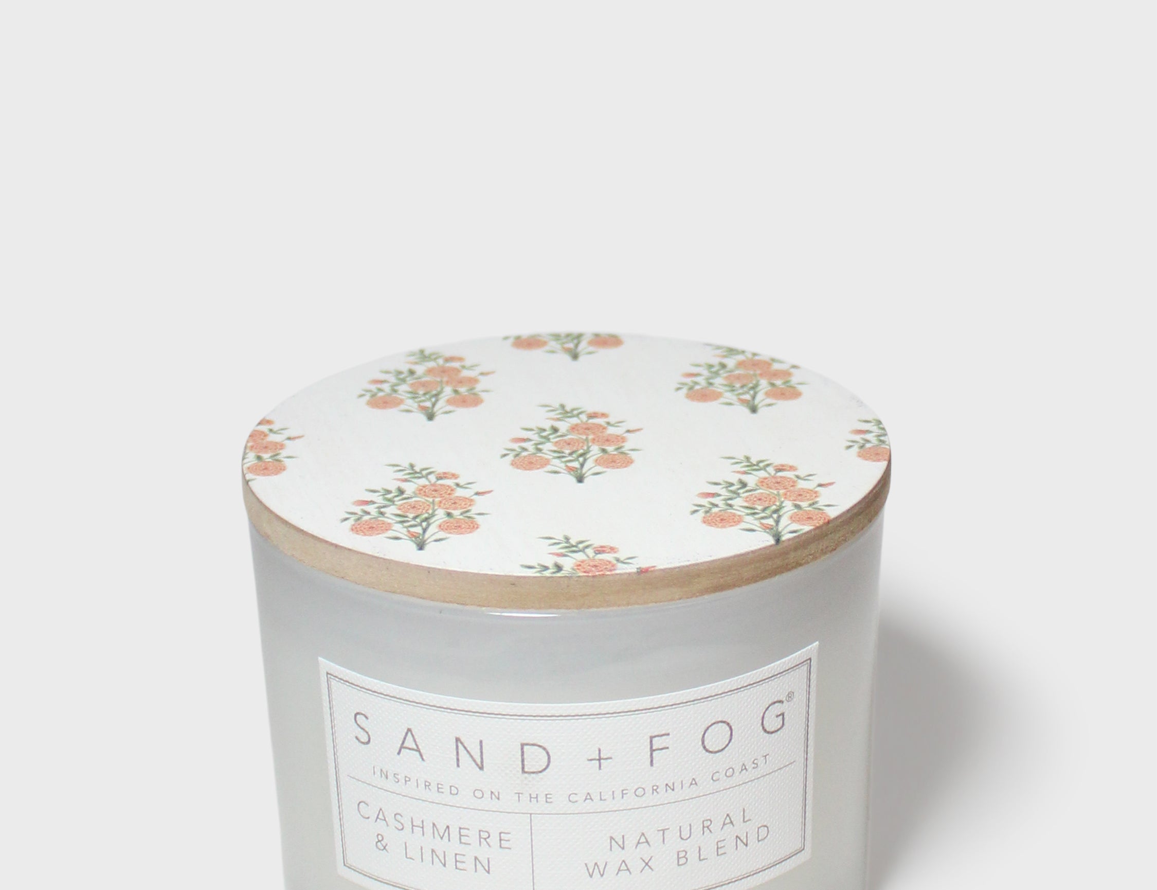 Scented candle jar with floral top and Sand + Fog wax blend label