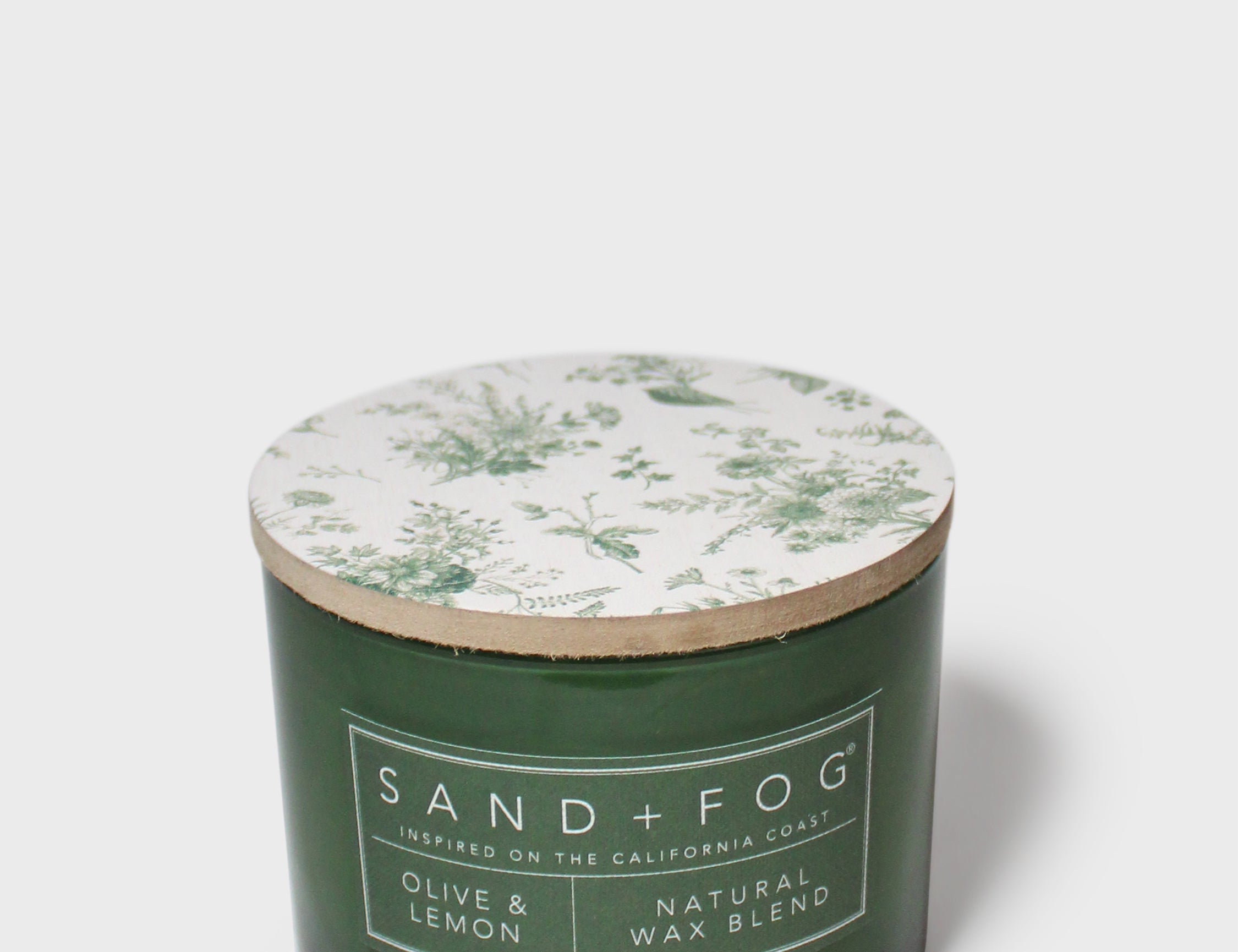 Green glass scented candle with botanical-printed lid and Sand+Fog label