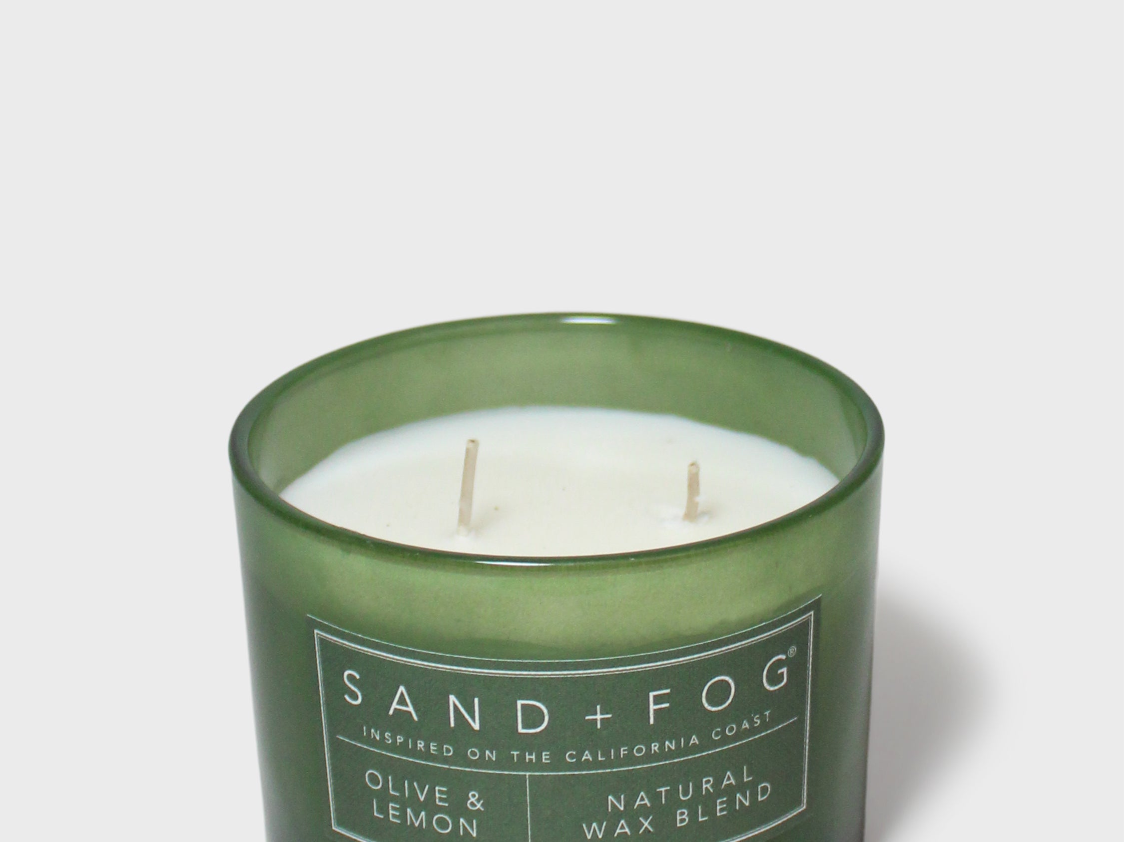 Green glass scented candle with twin wicks and Sand+Fog label