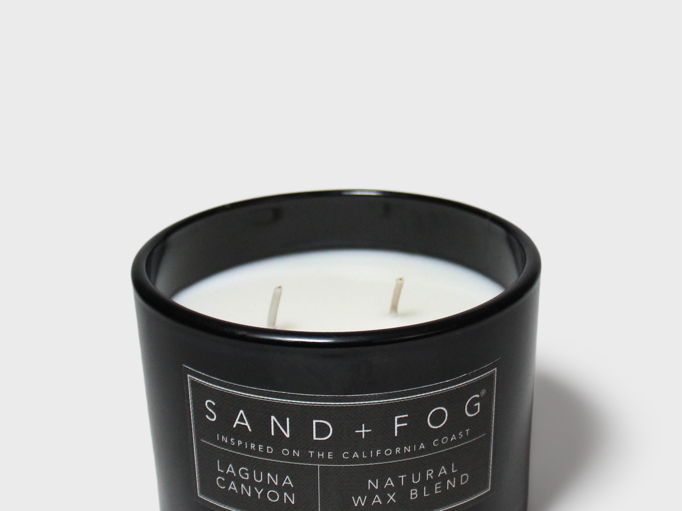 Scented candle in black glass jar with label and visible wax and wick