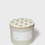 Scented candle with cream floral lid and Sand + Fog Sweet Lemon label