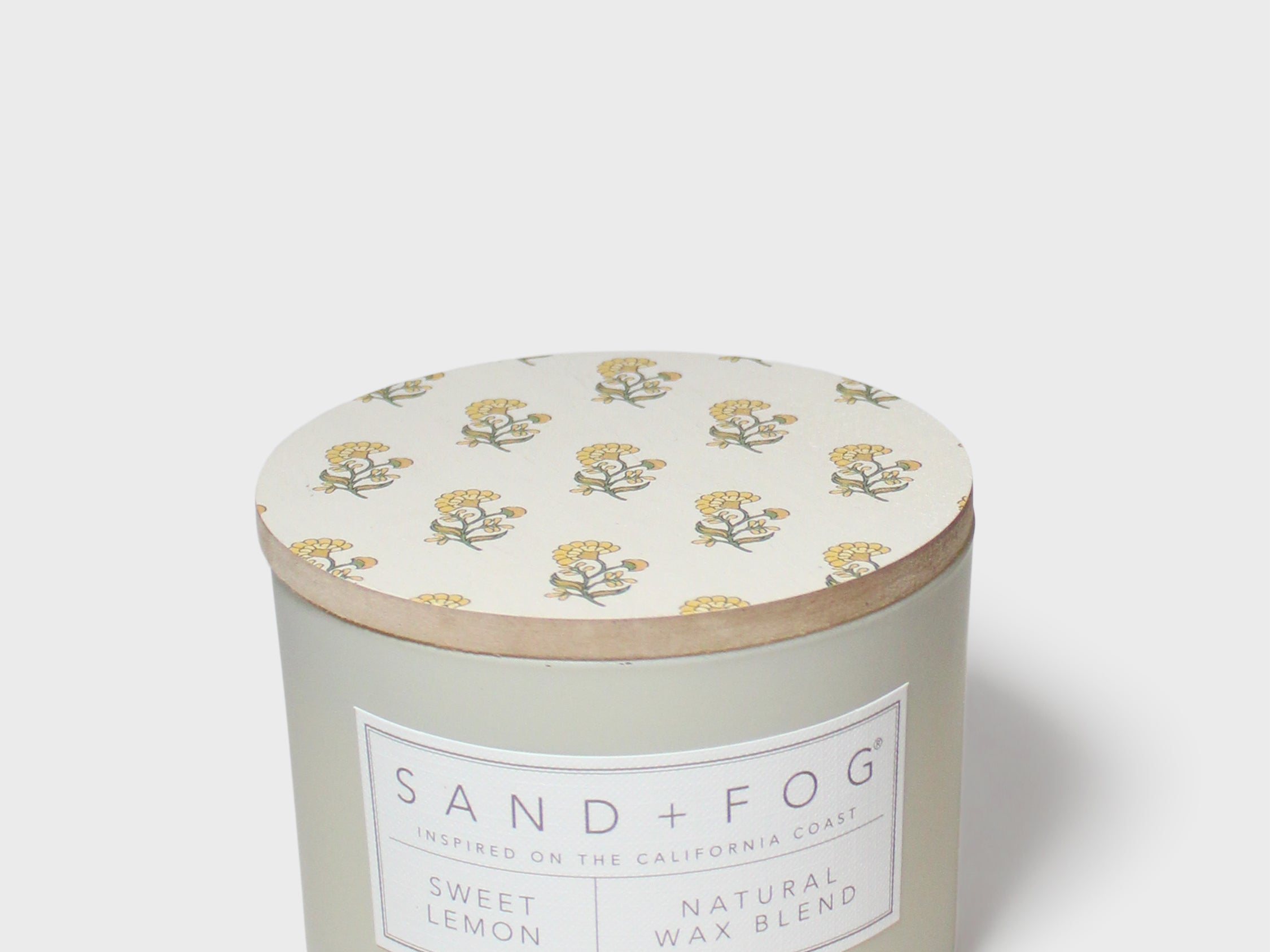 Scented candle with cream floral lid and Sand + Fog Sweet Lemon label