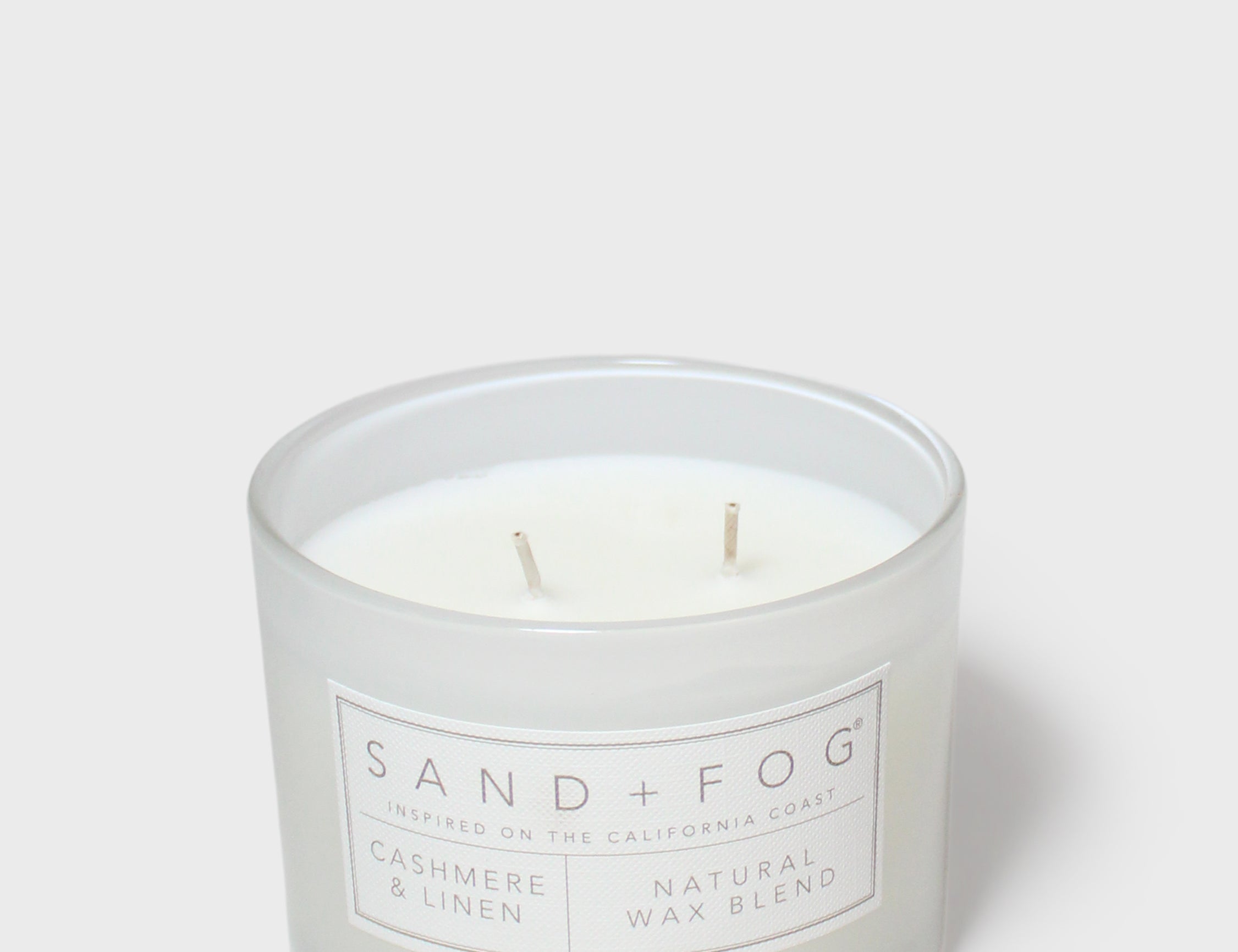 Clear glass jar scented candle with two wicks and Sand + Fog label