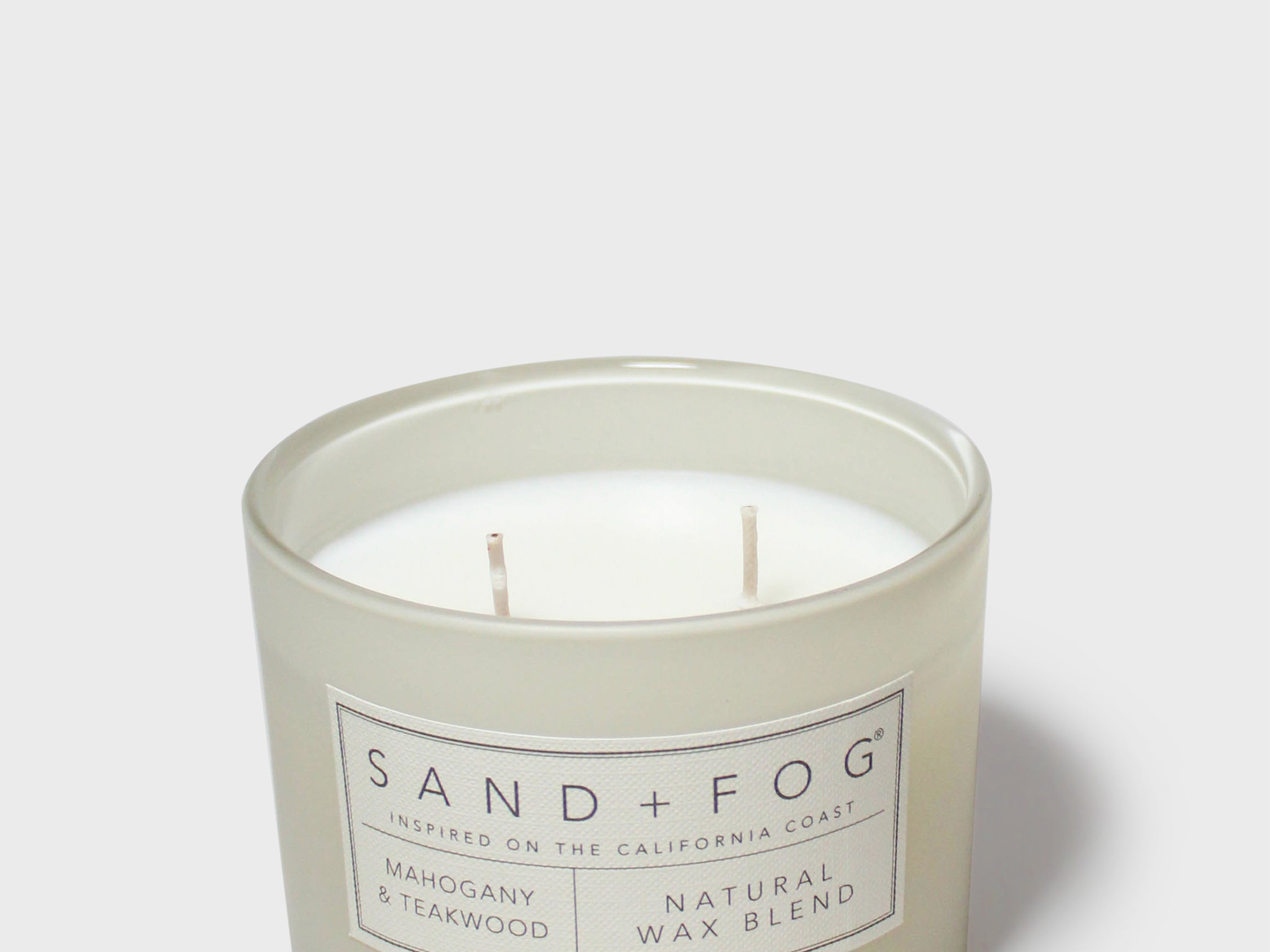 Scented candle in frosted glass jar with Sand+Fog label and two wicks