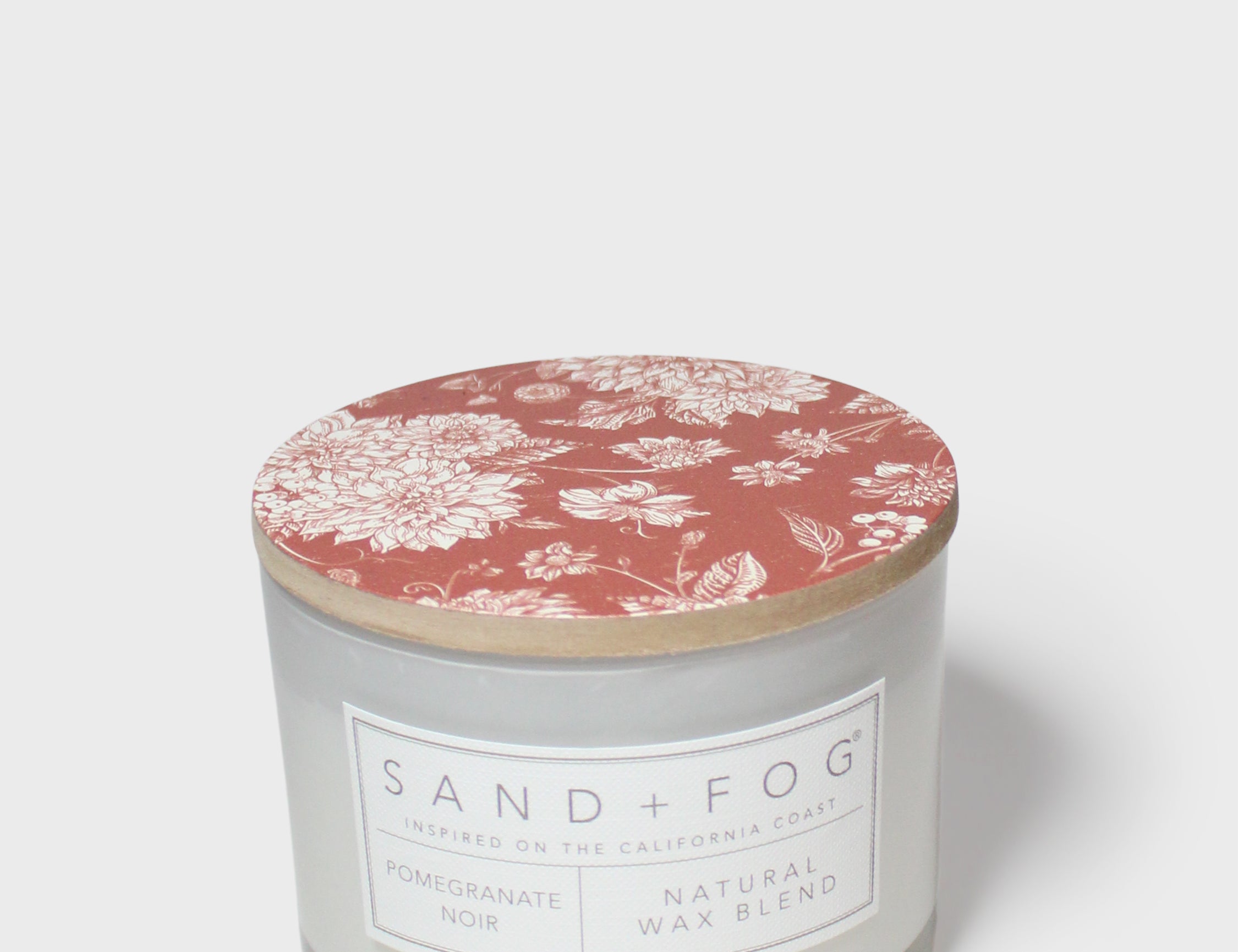 Scented candle in glass jar with red floral lid and “SAND+FOG” label