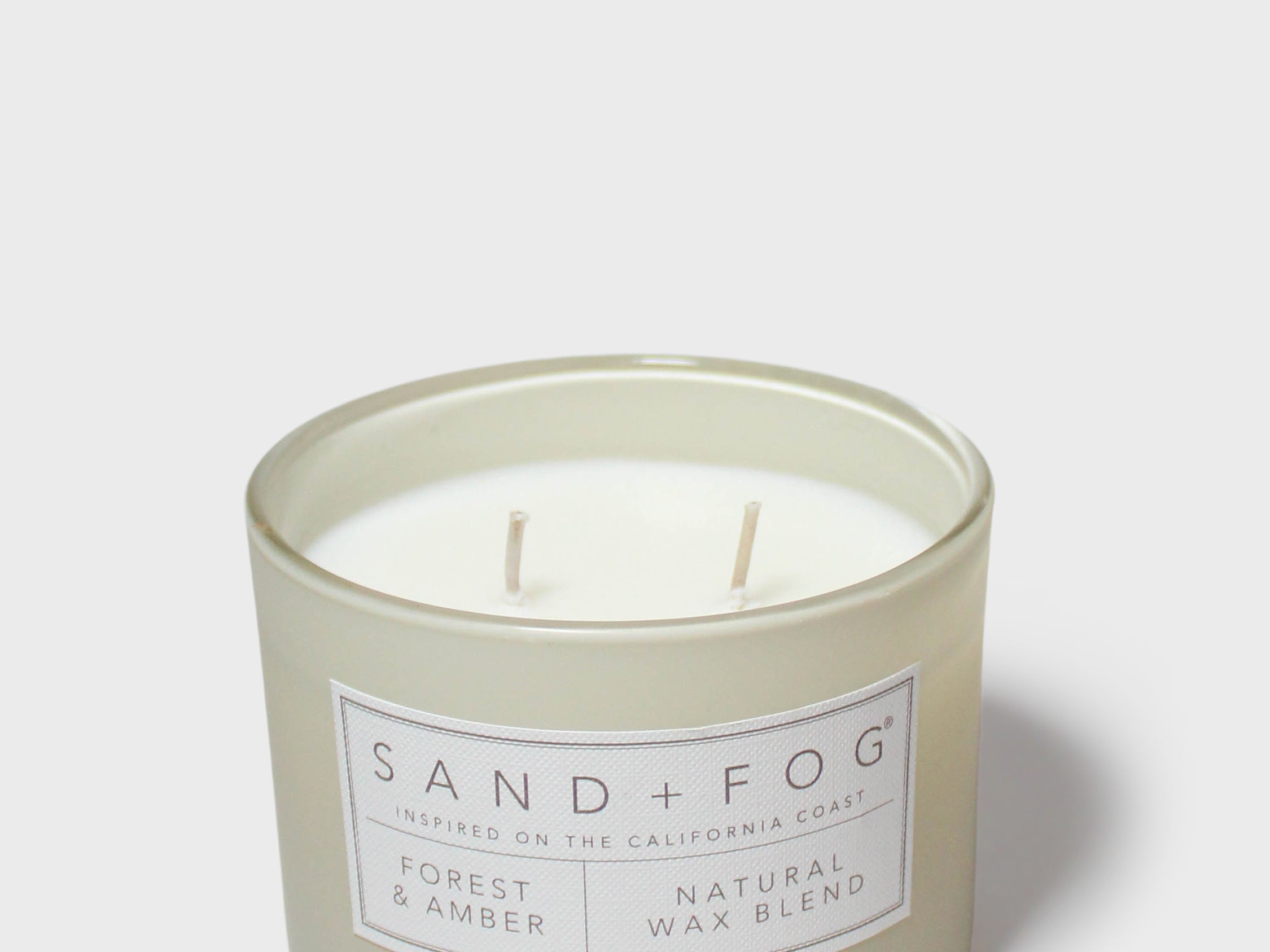 Scented candle in pale gray-green jar, two wicks visible through clear glass