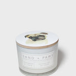 Scented candle lid with pug artwork and Sand + Paws label on glass jar