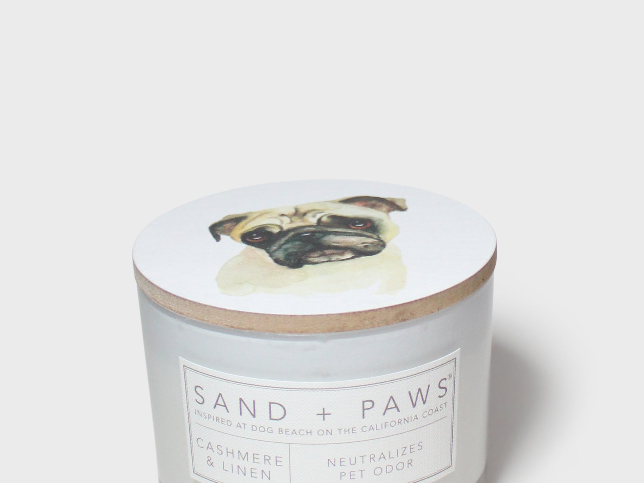 Scented candle lid with pug artwork and Sand + Paws label on glass jar