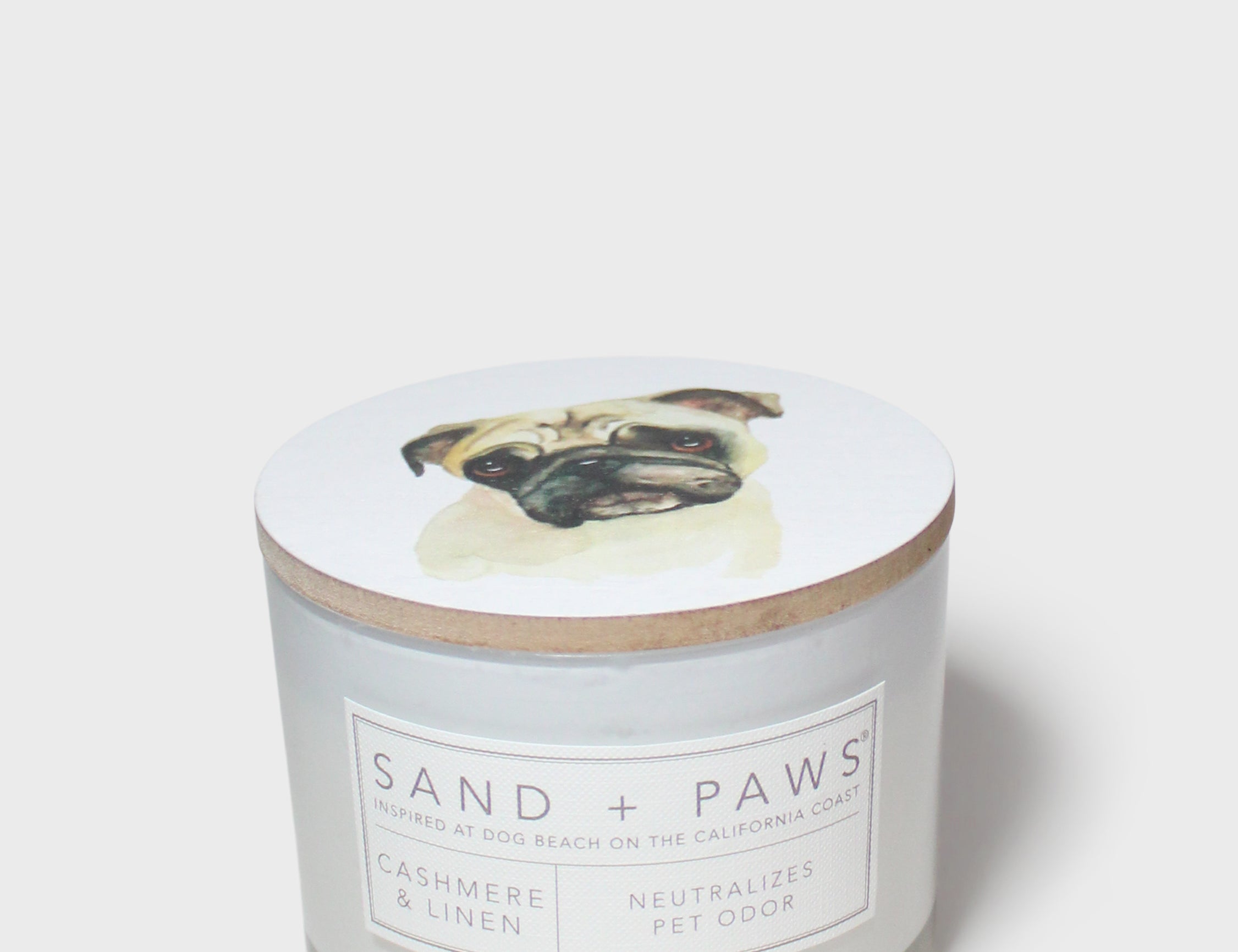Scented candle lid with pug artwork and Sand + Paws label on glass jar