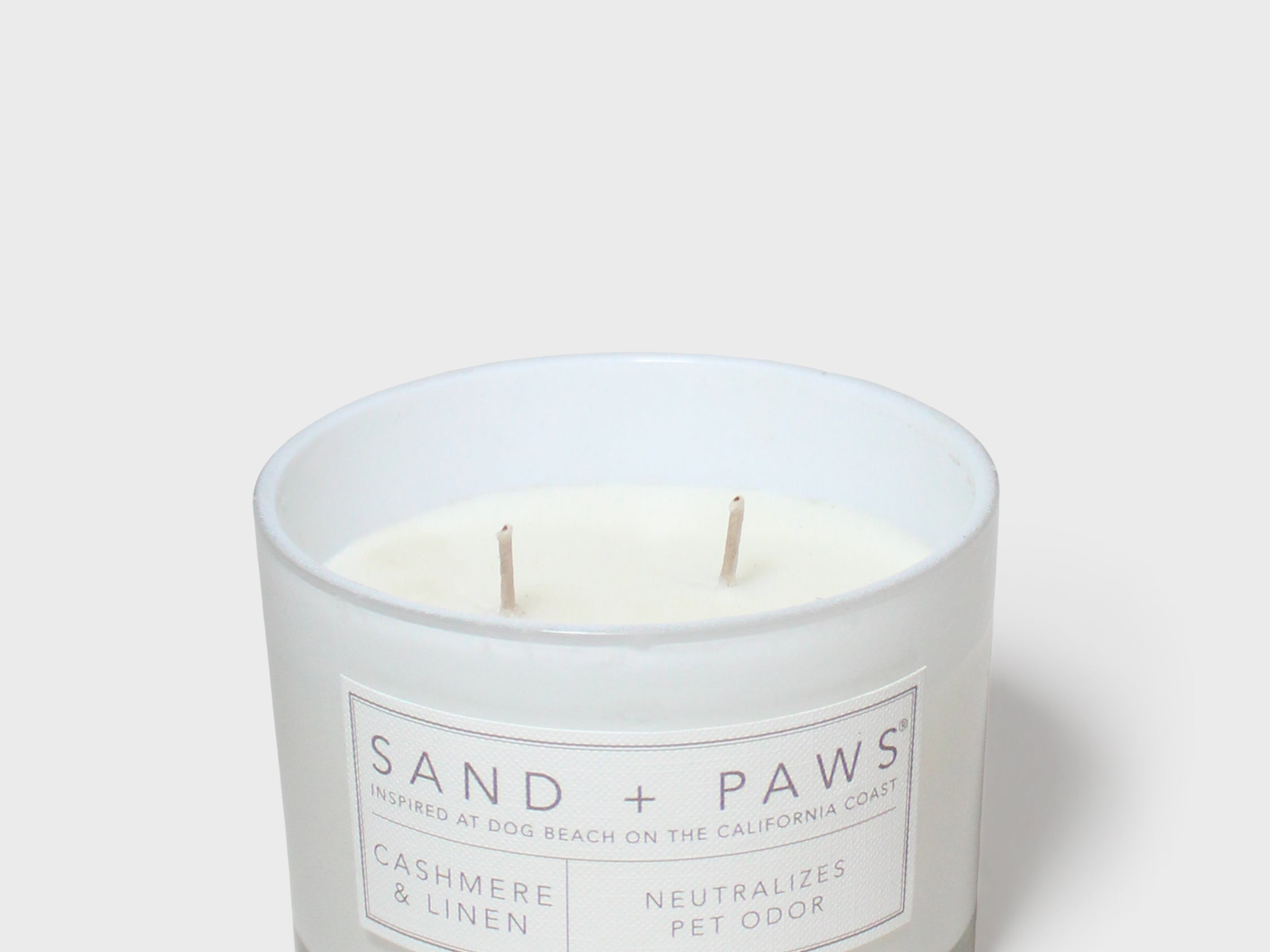 Scented candle in white glass jar with Sand + Paws label and two wicks